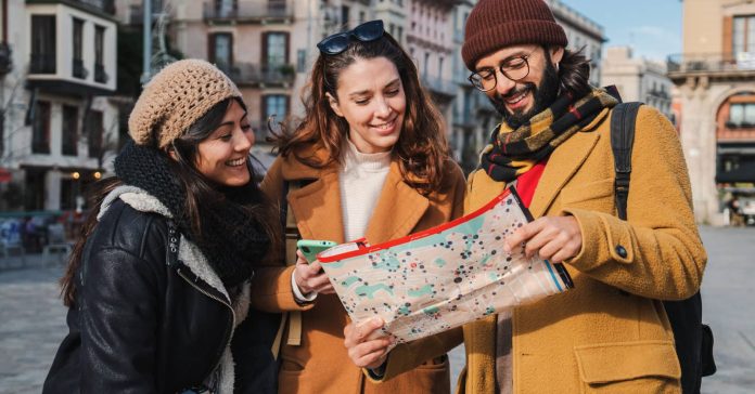 Group of tourists reading a map to found the location of a european monument. Three young travelers watching a guide looking directions visiting Barcelona city in a journey trip. Friends sightseeing. High quality photo